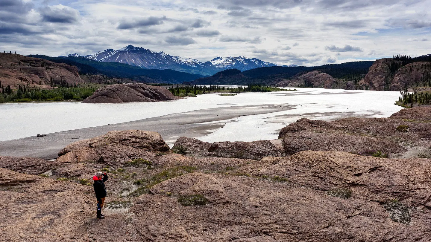 A man standing on a rock overlooking a lake and mountains.