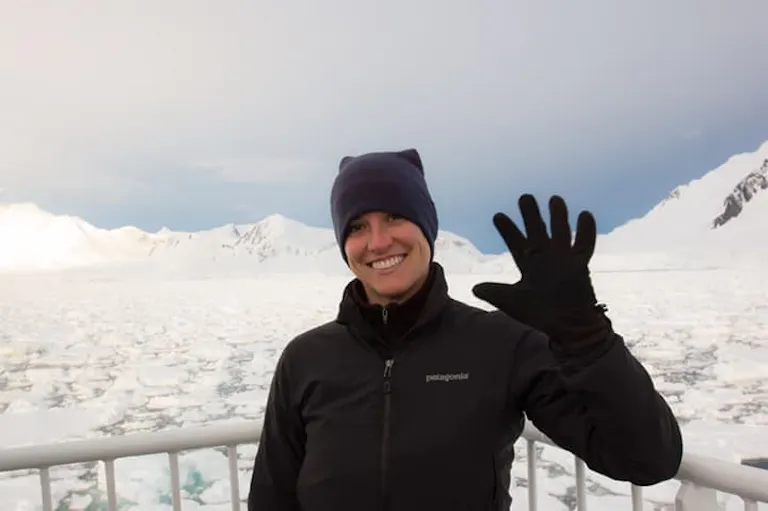 a solo traveler beaming and outdoors on the balcony of a polar cruise ship