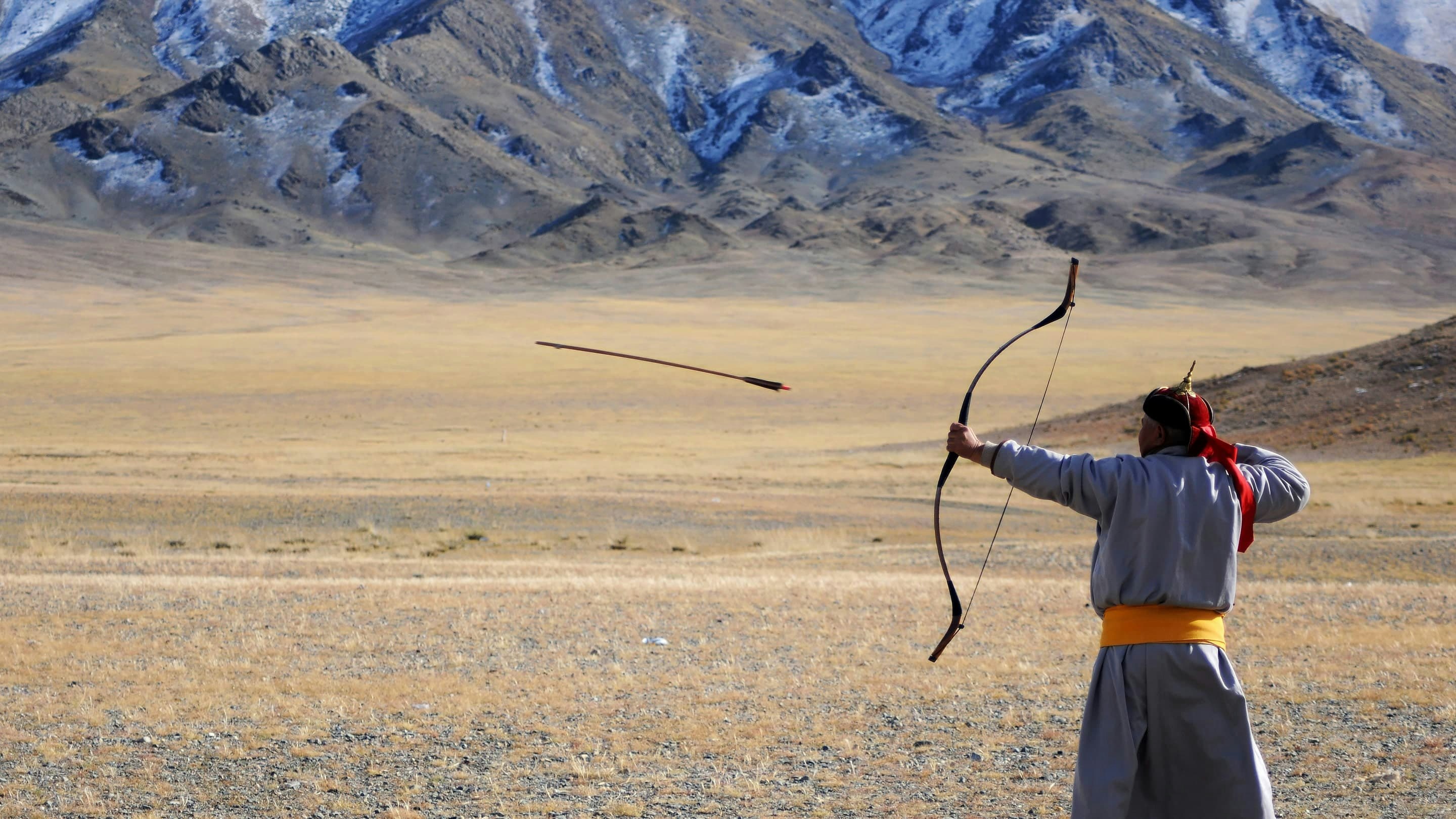 A man with a bow and arrow in the desert.