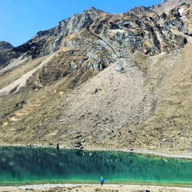 A man is standing near a lake in the mountains.