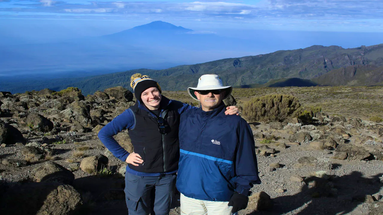 Two people standing on top of a mountain with a view of mt kilimanjaro.