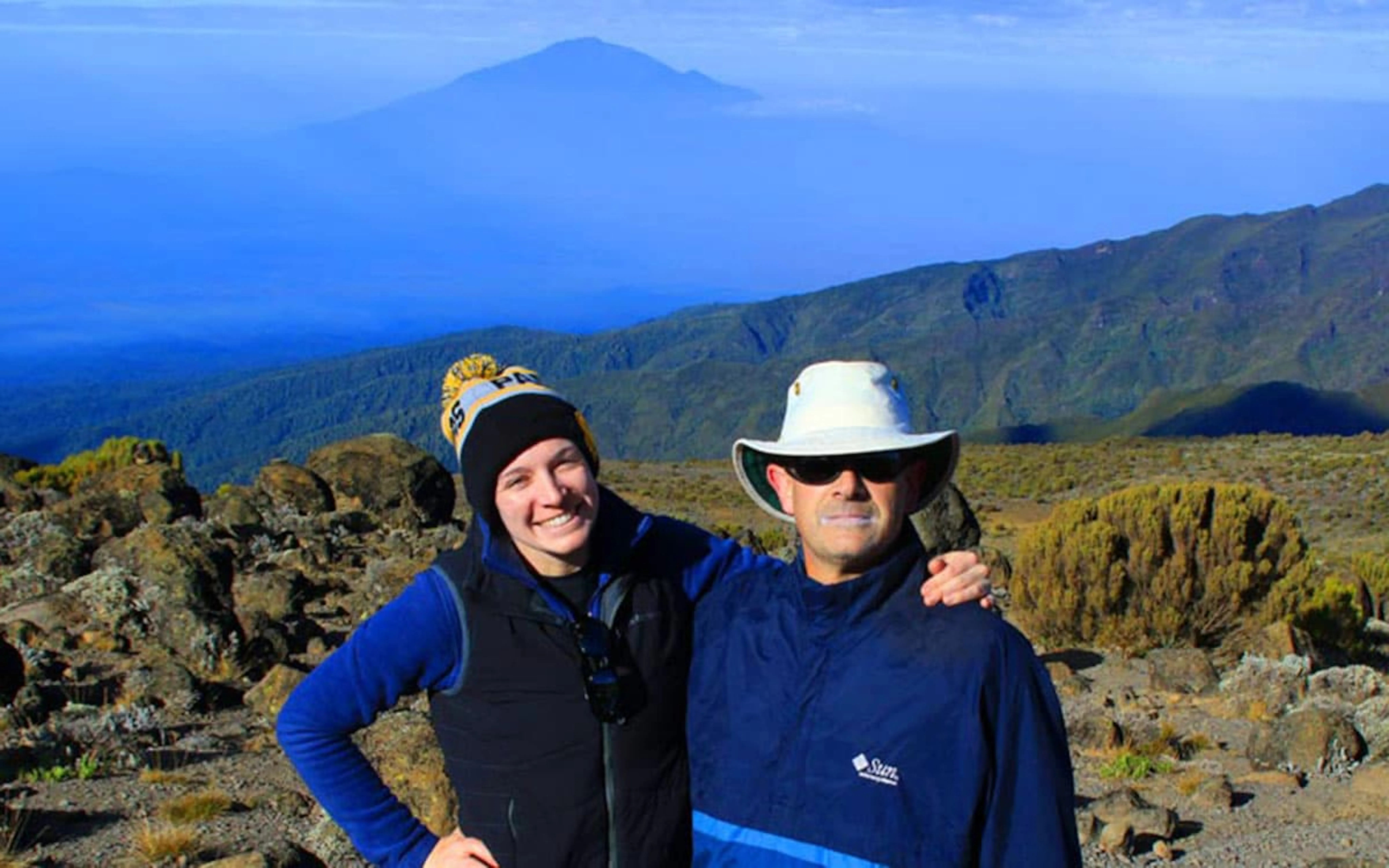 Two people standing on top of a mountain with a view of mt kilimanjaro.