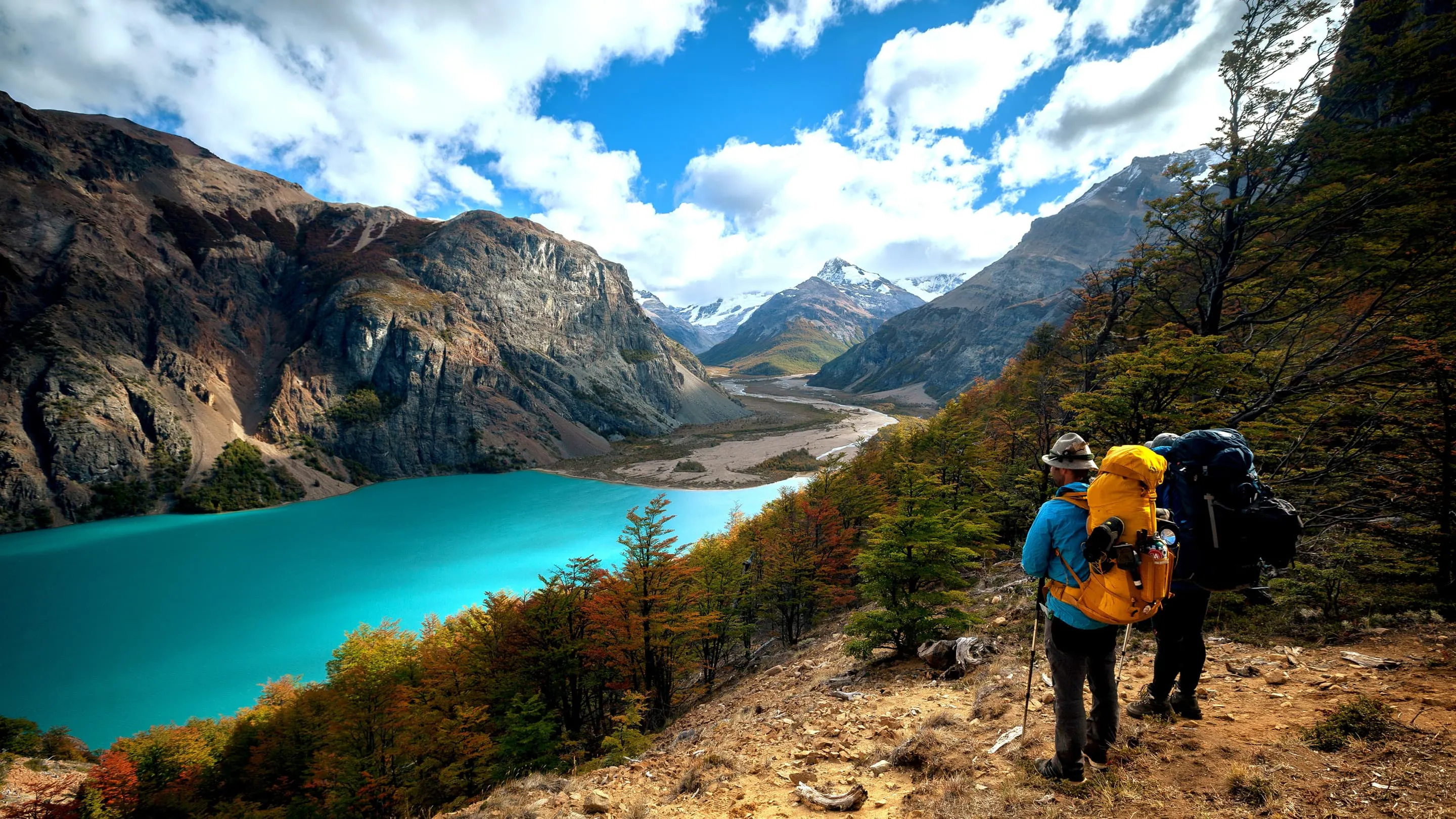 Two hikers looking at a blue lake in the mountains.