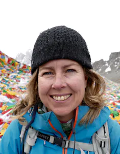 A woman smiling in front of a mountain of prayer flags.