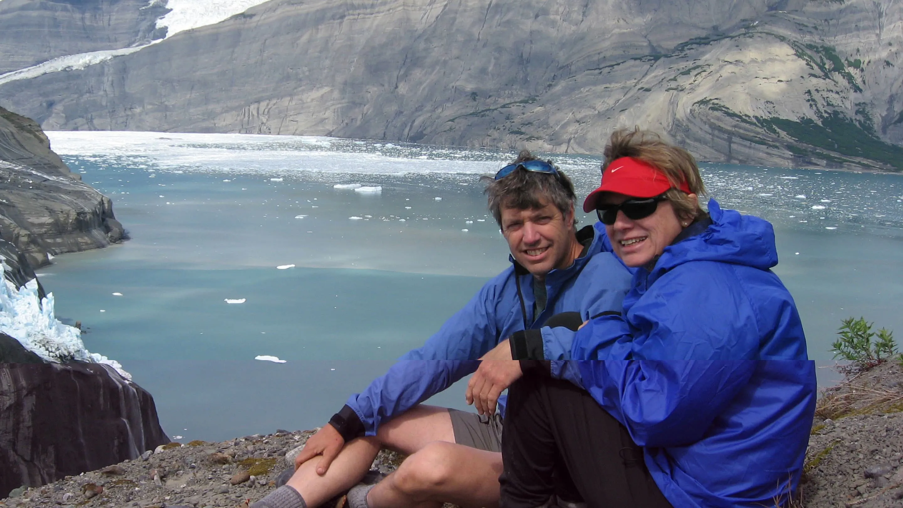 Two people sitting in front of a glacier.