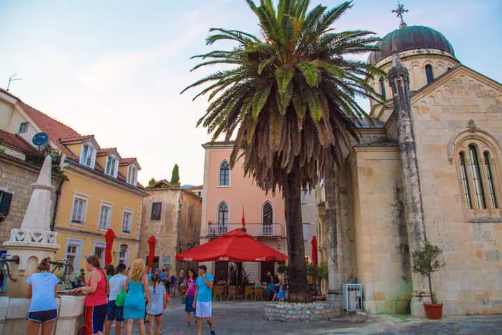 A group of people walking down a cobblestone street with a palm tree.