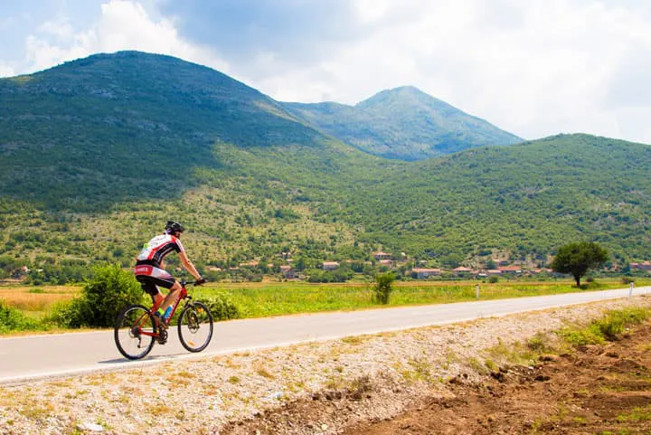 A cyclist rides down a road with mountains in the background.