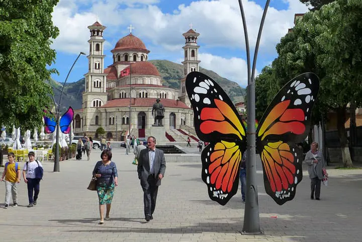 People walk past a large butterfly sculpture in front of a church.
