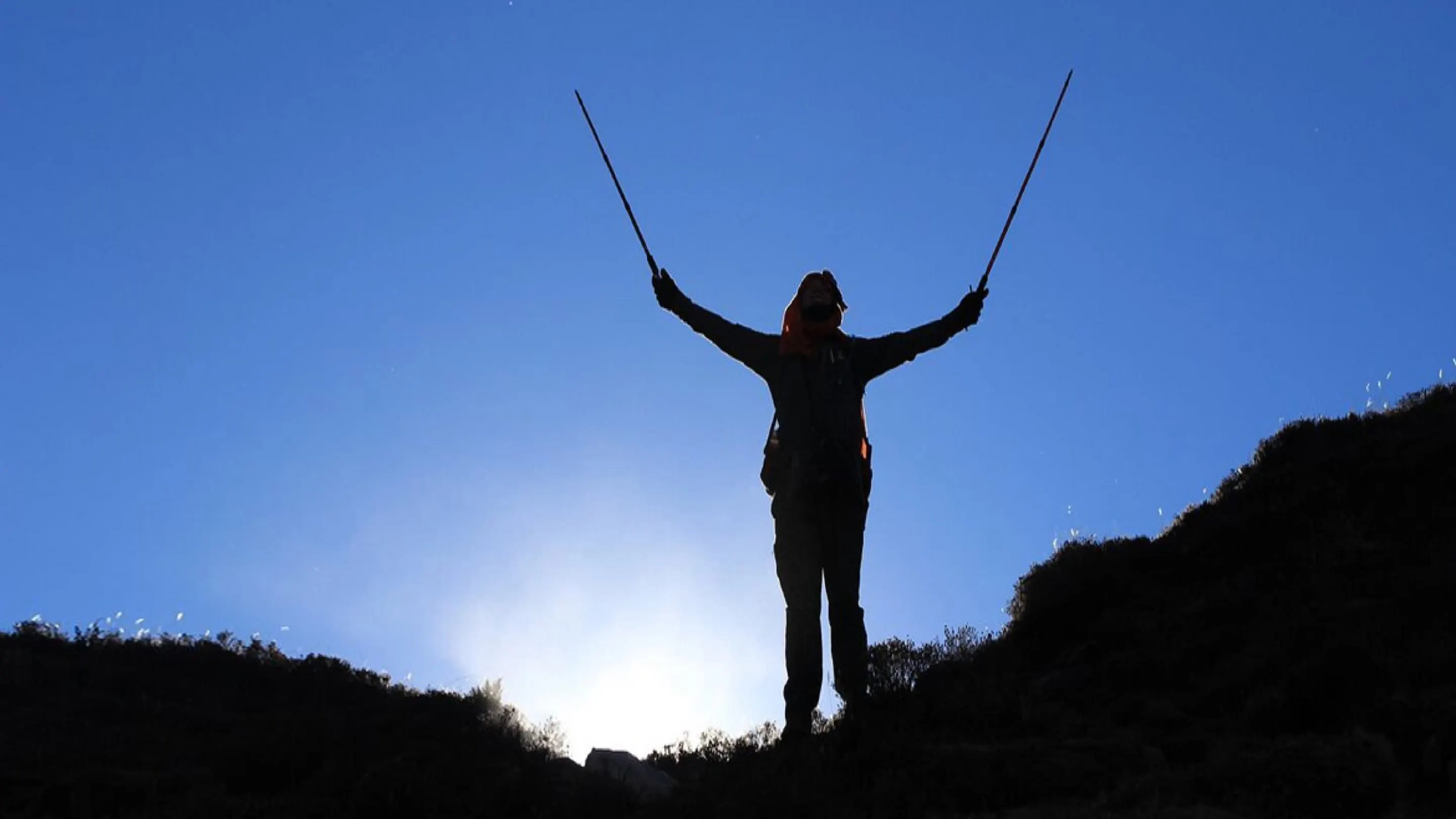 A silhouette of a person standing on top of a mountain.