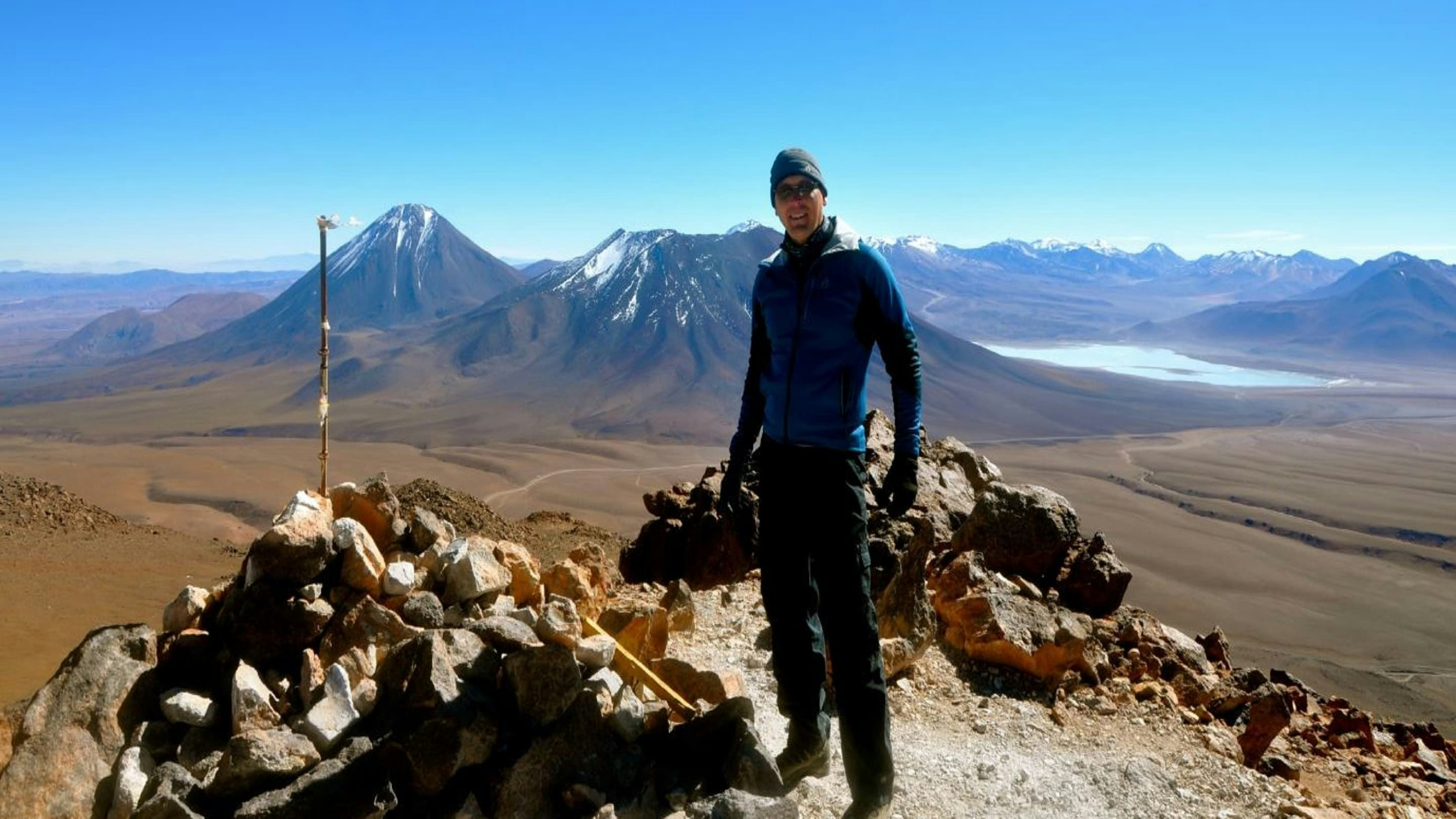 A man standing on top of a mountain with mountains in the background.