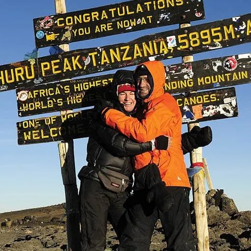 Two people hugging in front of a sign at the summit of mt kilimanjaro.
