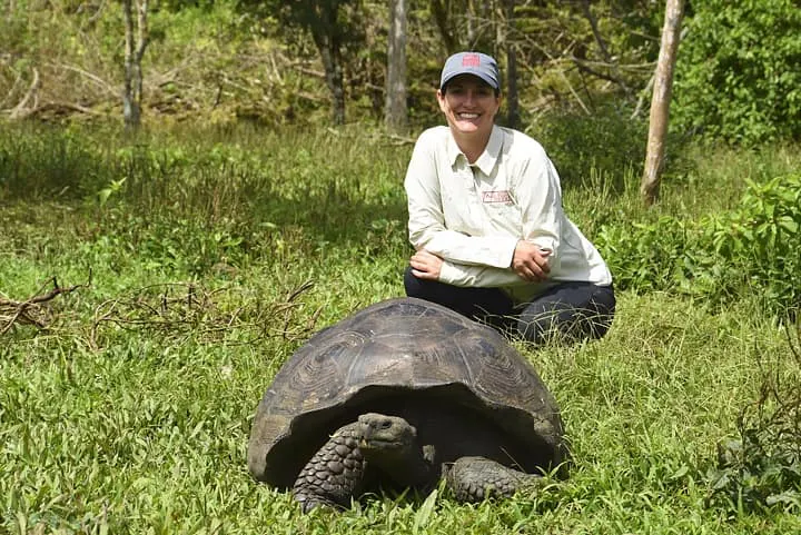 A woman kneeling down next to a giant tortoise.