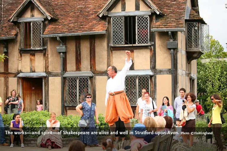 A English man in white clothes and orange pants is orating from Shakespeare