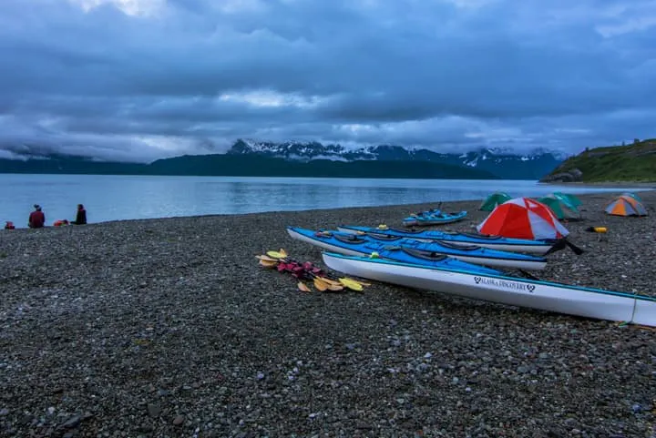 Kayaks and tents on a beach with mountains in the background.