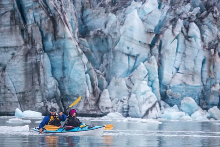 Two people in a kayak in front of a glacier.