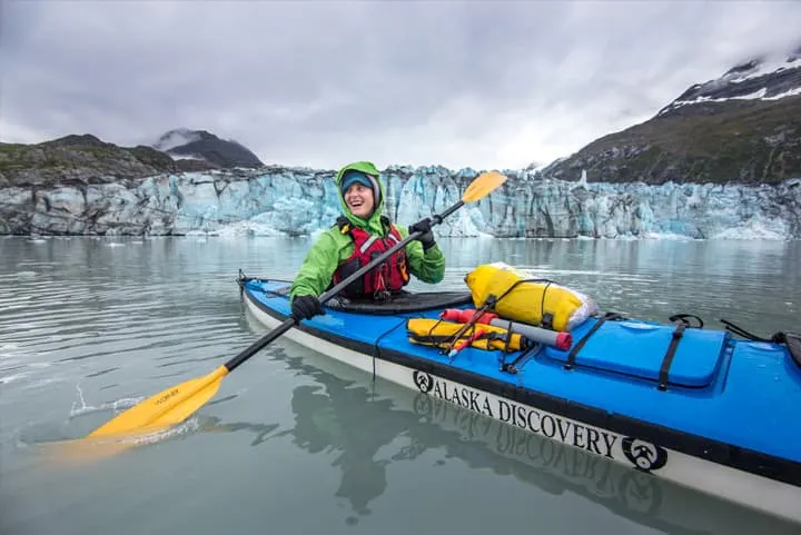 A woman in a kayak in front of a glacier.