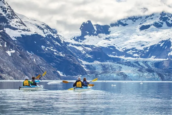 A group of people are kayaking in the water near a glacier.