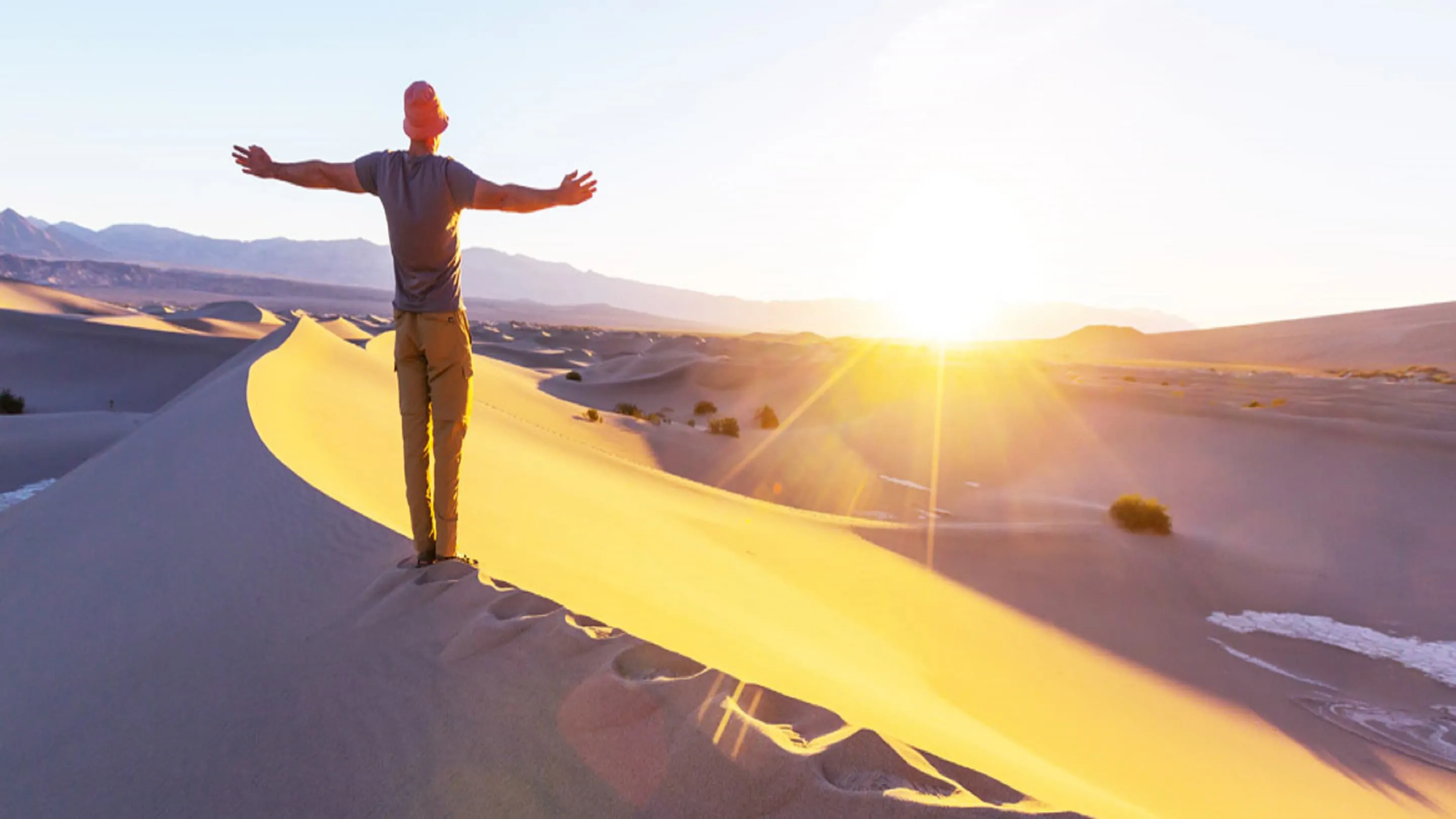 A man standing on top of a sand dune at sunset.
