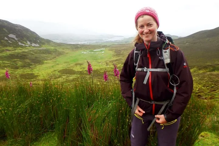 A woman is standing on a hill with a backpack.