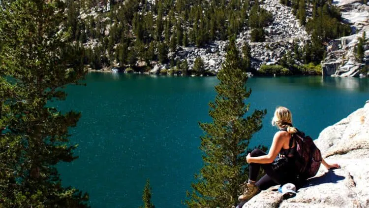 A woman sits on a rock overlooking a lake.