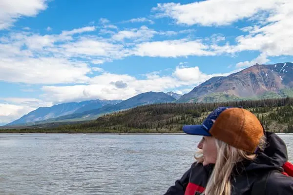A woman on a boat looking out over a body of water with mountains in the background.