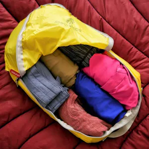 A yellow bag filled with clothes on a bed.