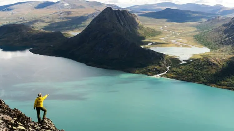 A man standing on top of a mountain overlooking a lake.