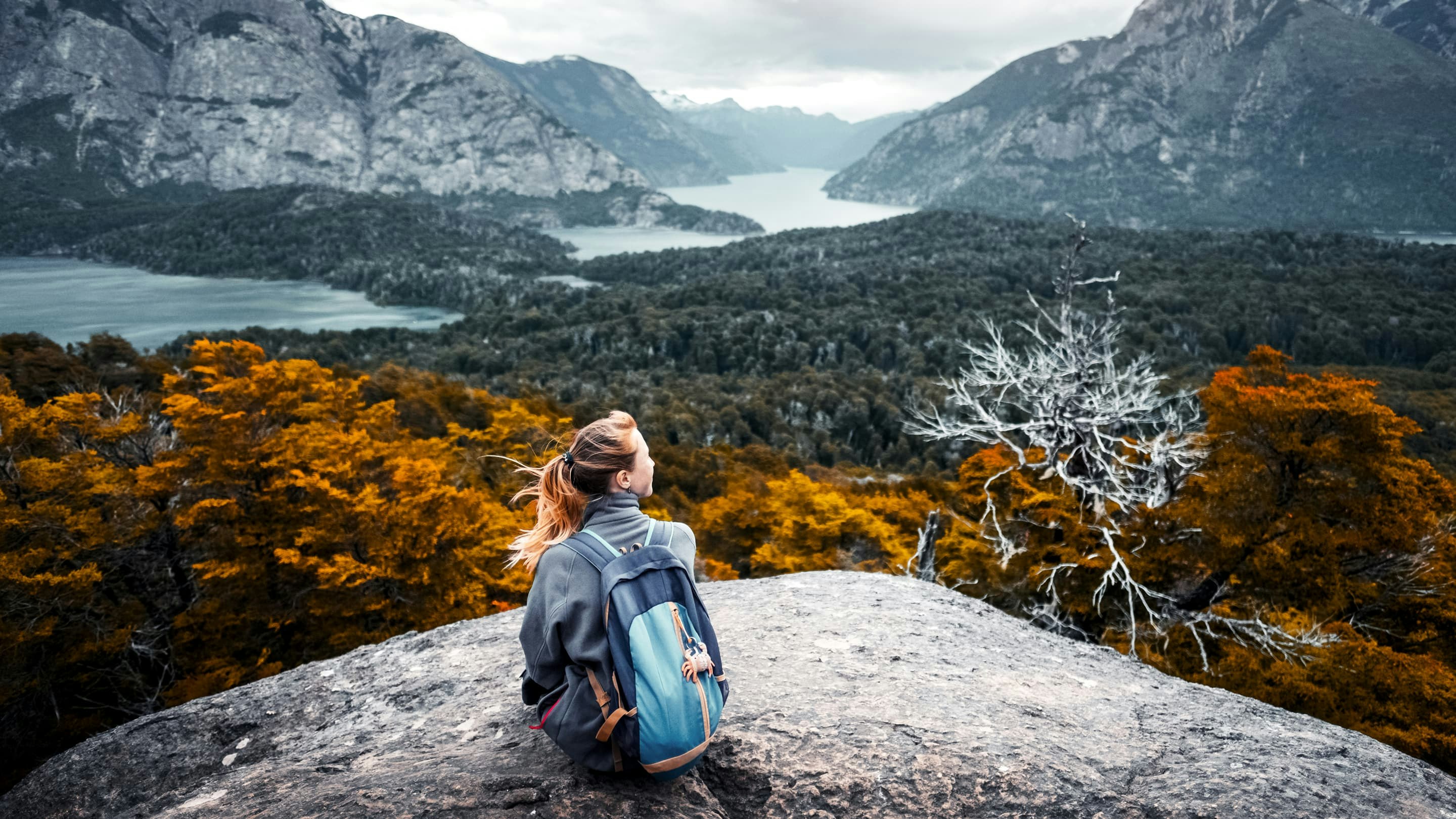 A woman sitting on top of a mountain overlooking a lake.