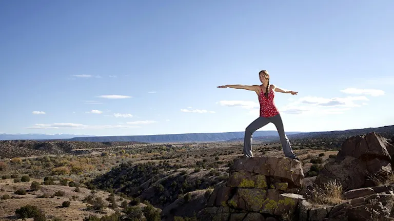 A woman standing on top of a rock with her arms outstretched.