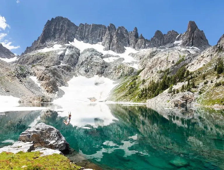 A person is standing in a lake surrounded by mountains.