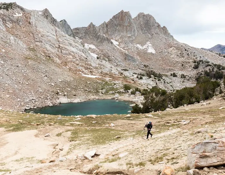 A hiker on a trail near a lake in the mountains.
