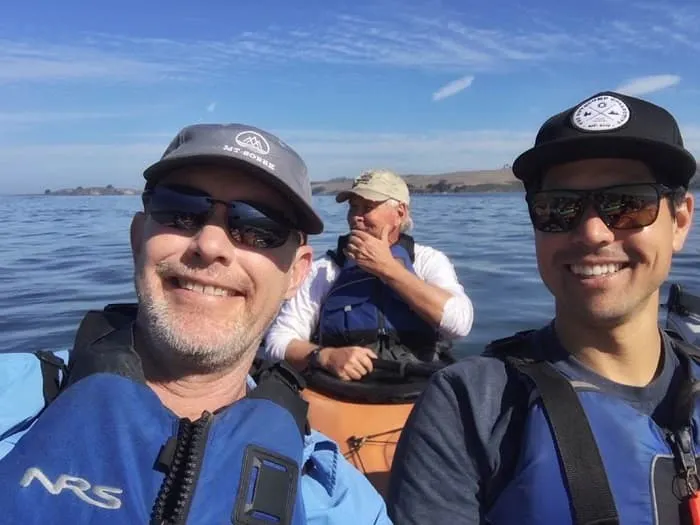 Three men on a kayak taking a selfie.