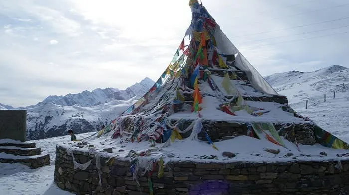 A snow covered stone structure with prayer flags on top.
