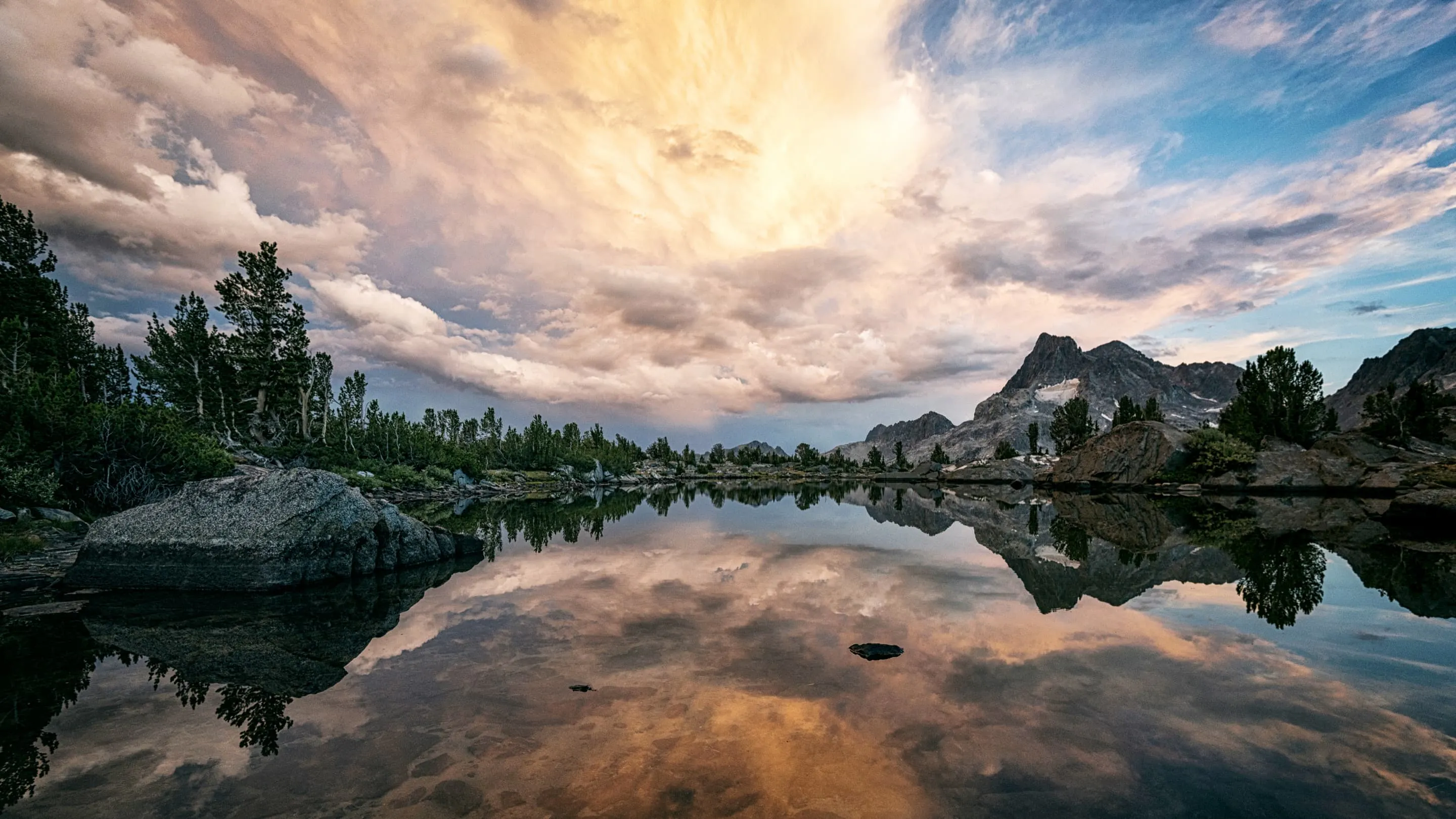 Clouds reflected in a lake with rocks and trees.