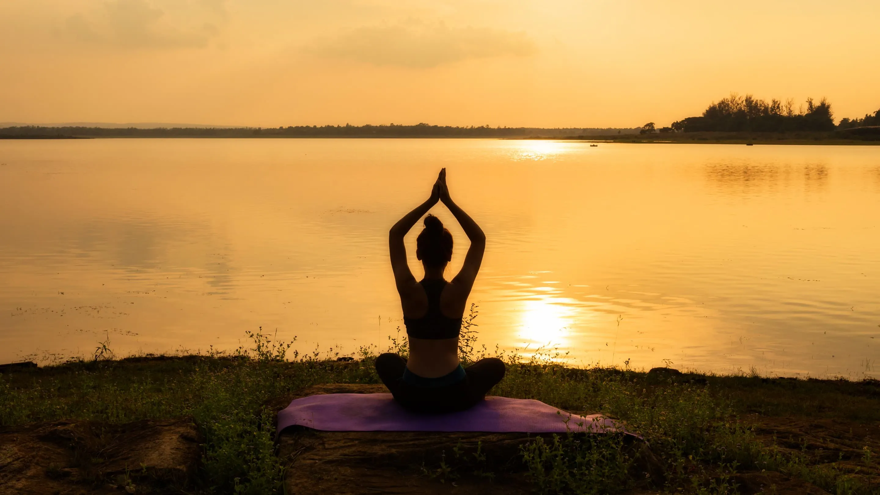 A woman is doing yoga in front of a lake at sunset.