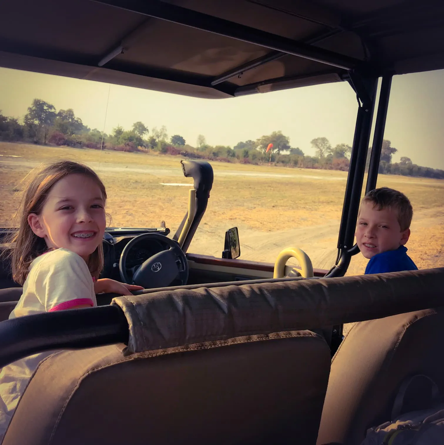 Two children sitting in the driver's seat of a vehicle.