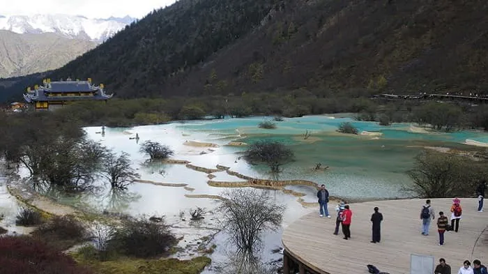 A group of people standing on a wooden platform near a lake.