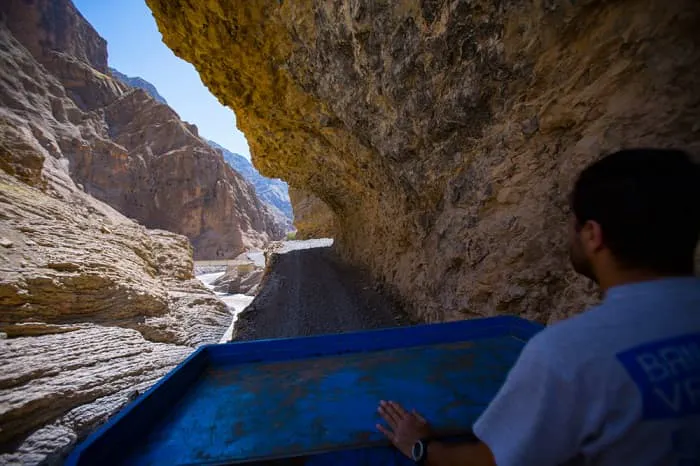 A man in a blue truck driving through a narrow canyon.