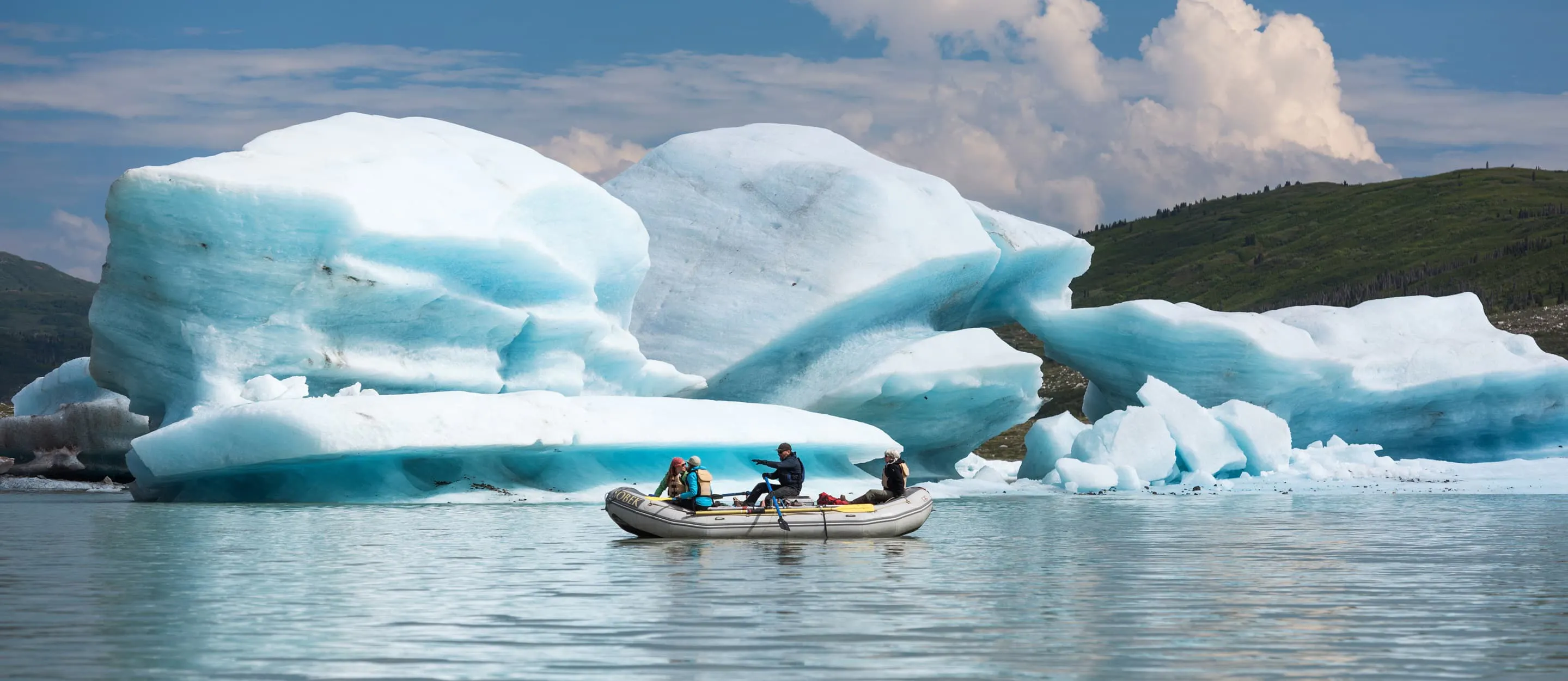 Two people on a rafting trip, with icebergs in the background.