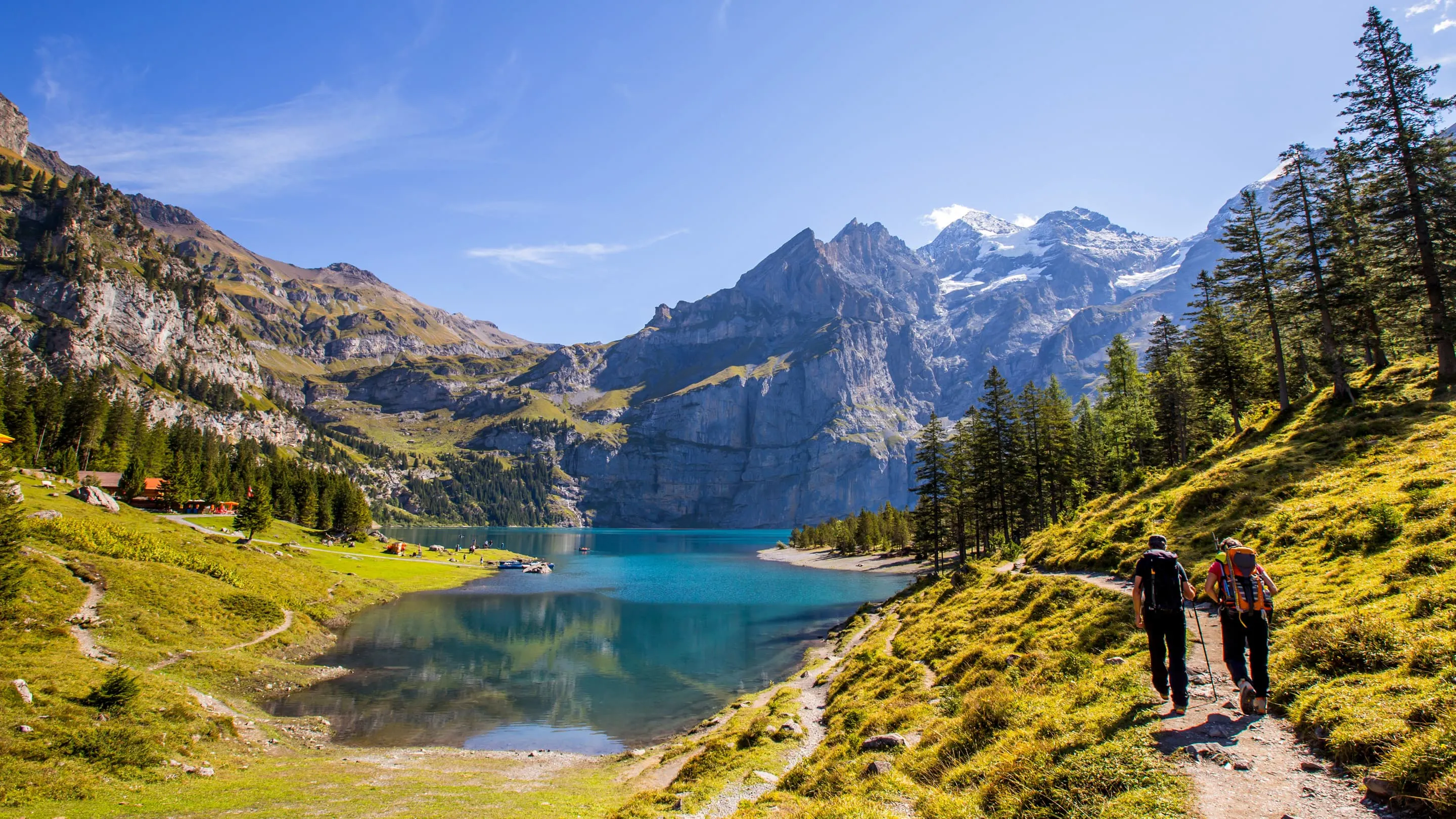 Two people walking on a path near a lake.