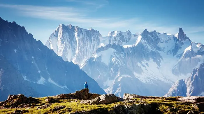 A person standing on top of a rock with mountains in the background.
