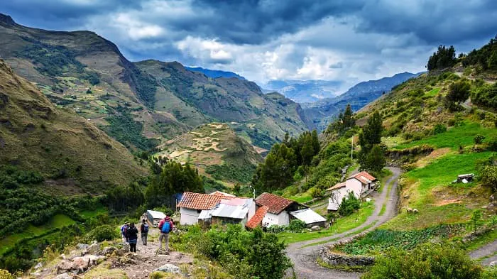 A group of people walking down a dirt road in the mountains.