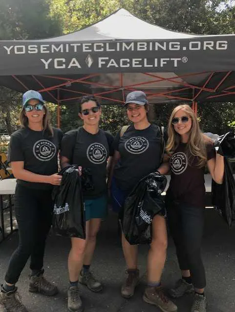 Four women standing under a tent with a sign that says yosemite climbing ymca facelift.