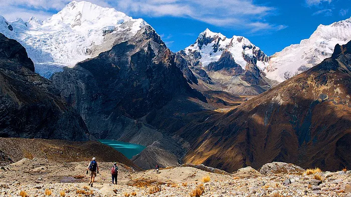 Two people walking along a rocky path with mountains in the background.