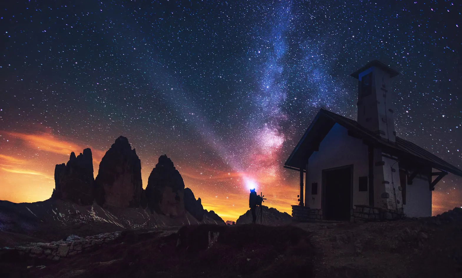 A person is standing in front of a mountain with the milky in the sky.