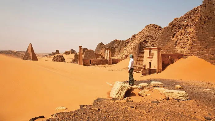 A man is standing in front of a sand dune.