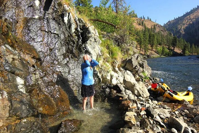 A man standing in the water next to a rocky cliff.