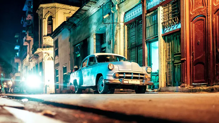 An old car is parked on a street at night.