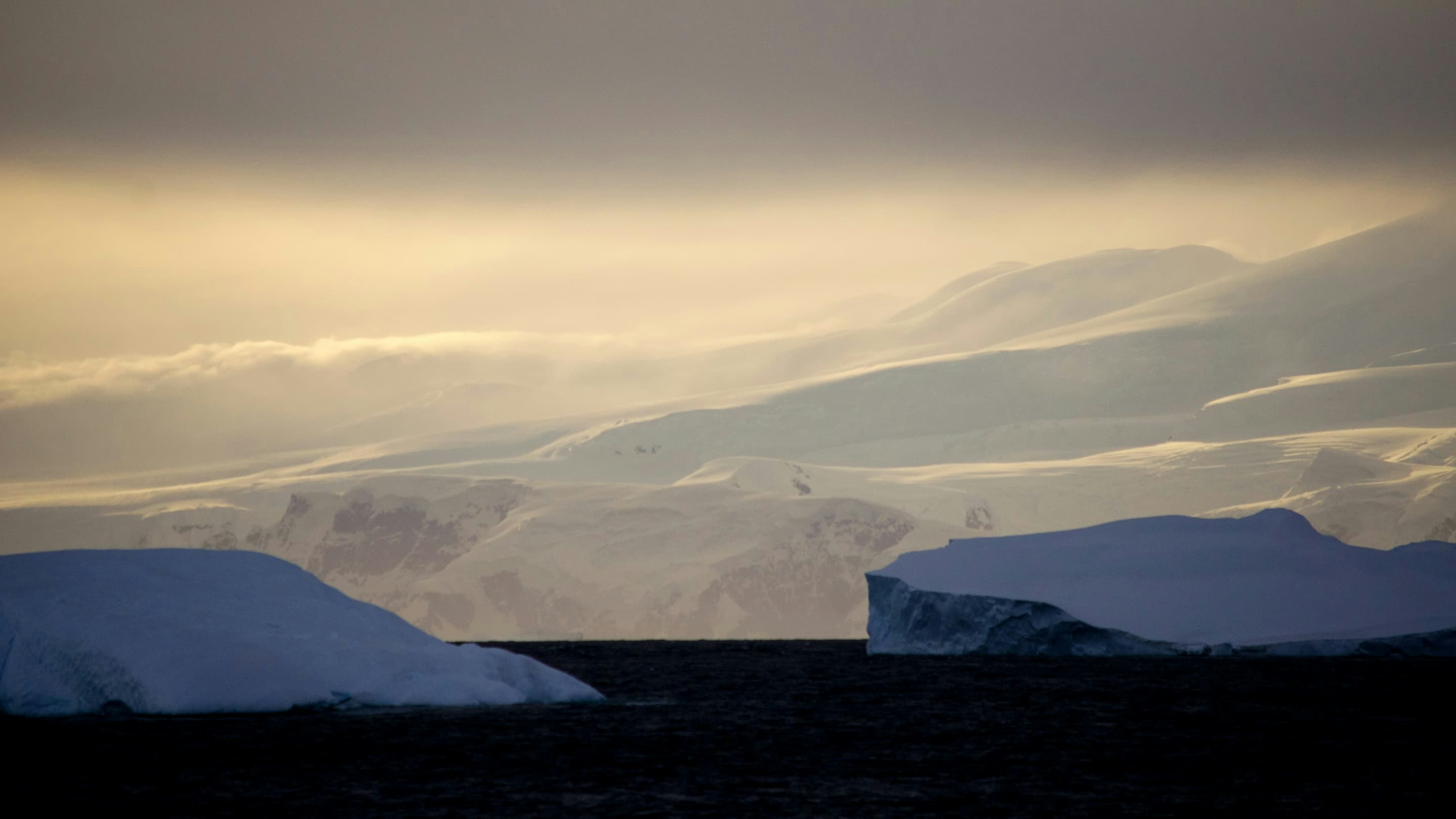 A group of icebergs in the ocean with a cloudy sky.