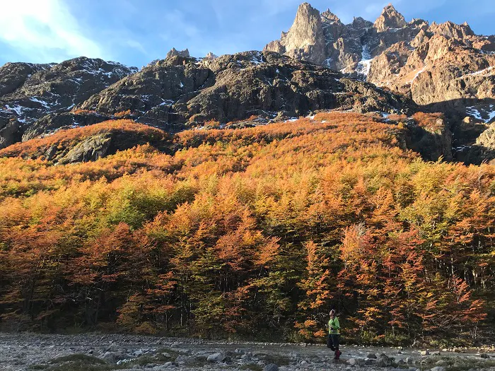 A person walking in front of a mountain with trees in the background.